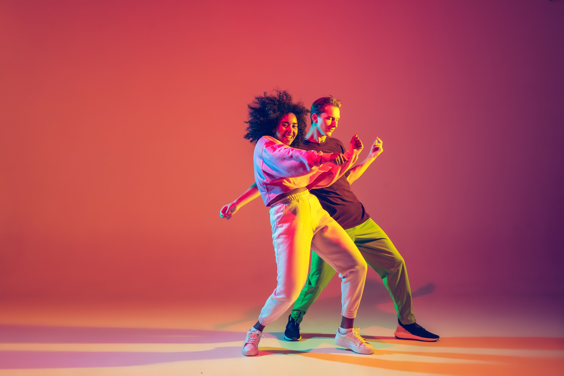 Stylish man and woman dancing hip-hop in bright clothes on gradient background at dance hall in neon light