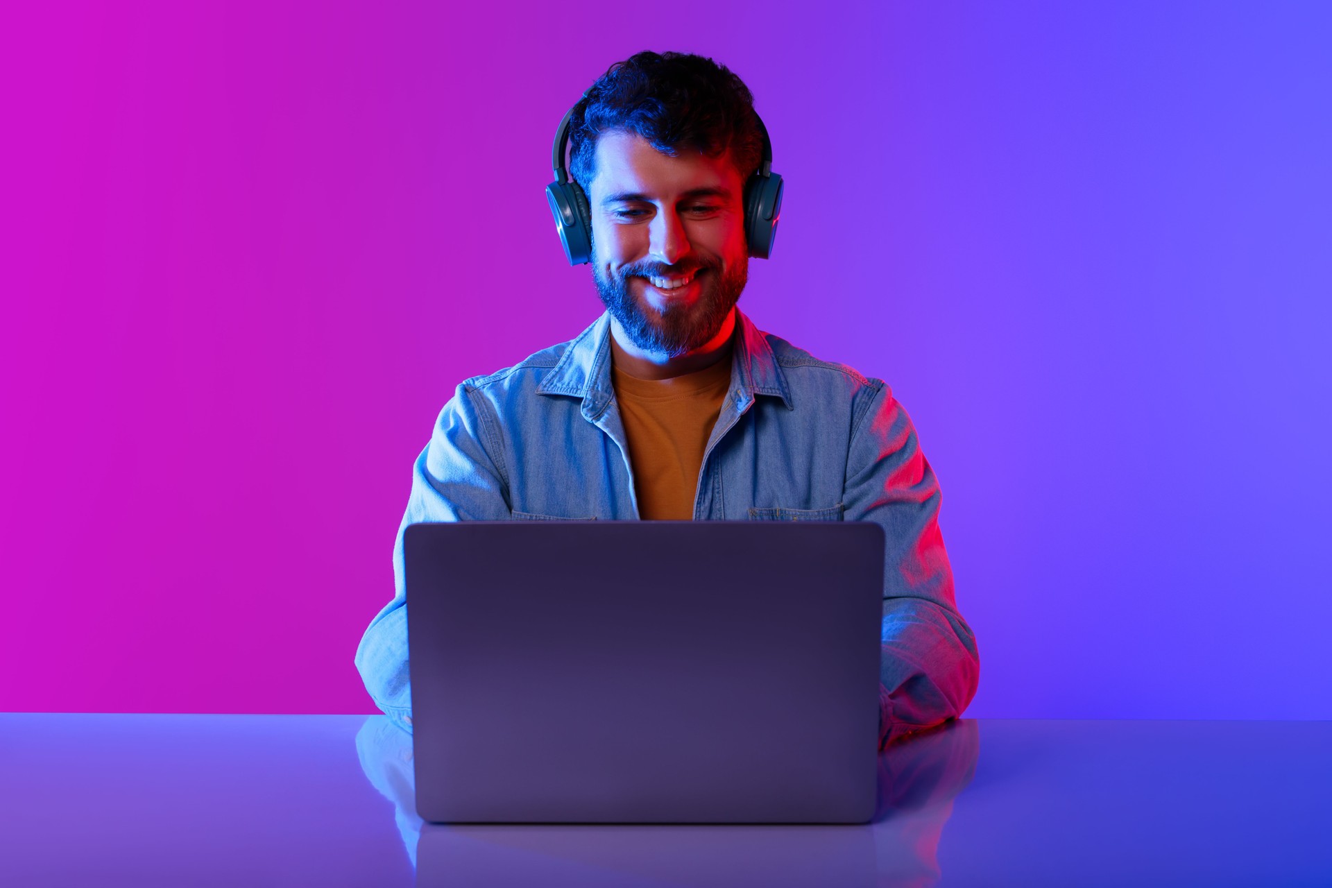 Happy Millennial Guy Wearing Headphones Browsing Internet On Laptop, Studio