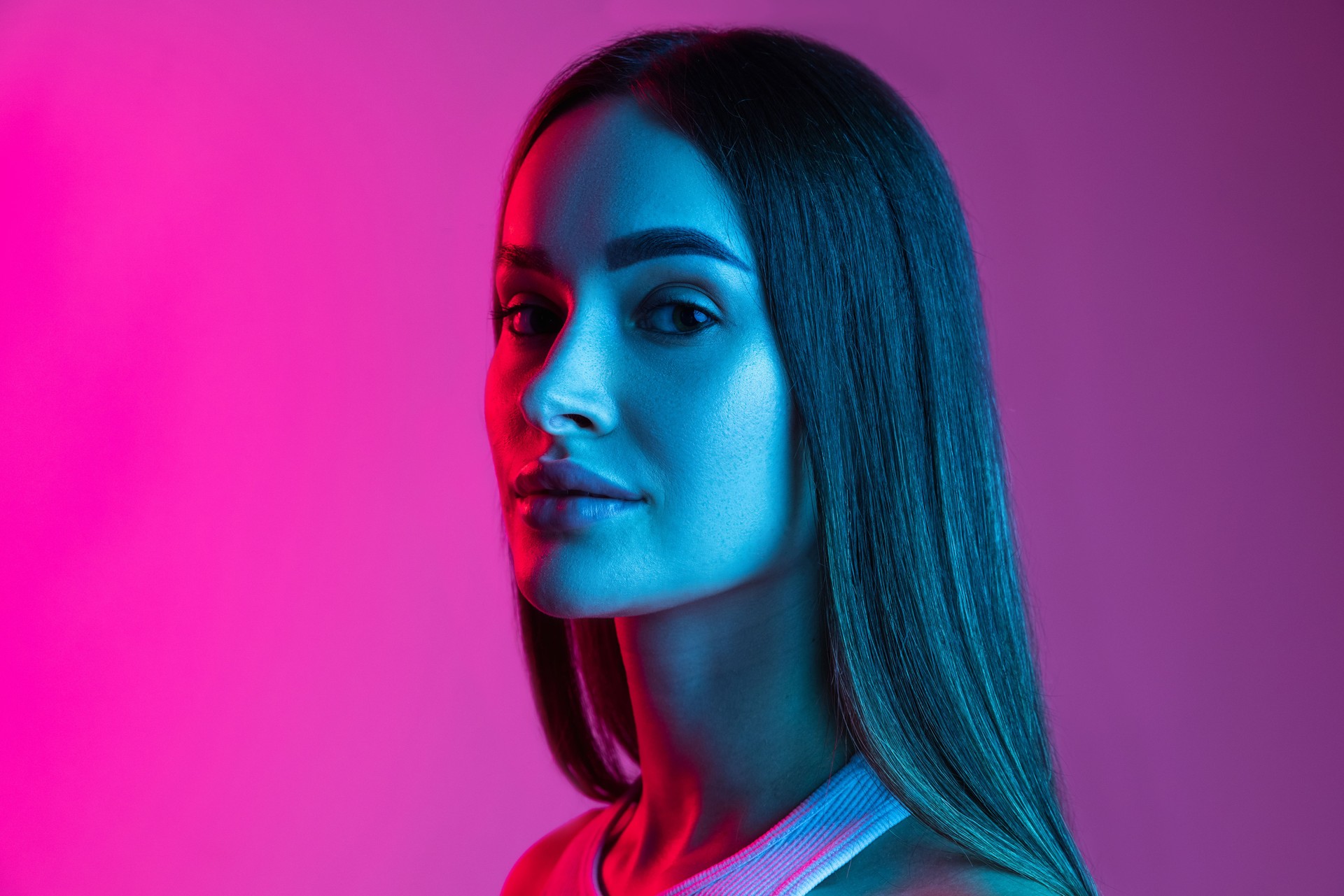 Side-viewed close-up portrait of young beautiful girl isolated on pink purple studio background